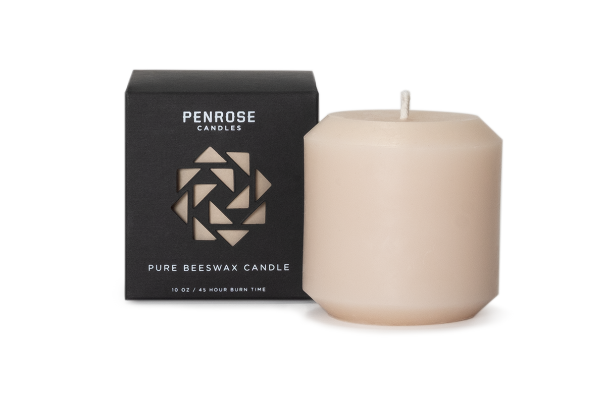 Nude beige beeswax pillar candle next to black Penrose Candles packaging box with geometric logo design