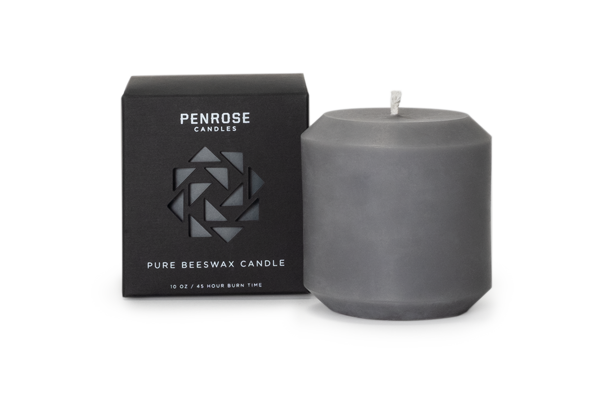 Slate gray beeswax pillar candle next to black Penrose Candles packaging box with geometric logo design